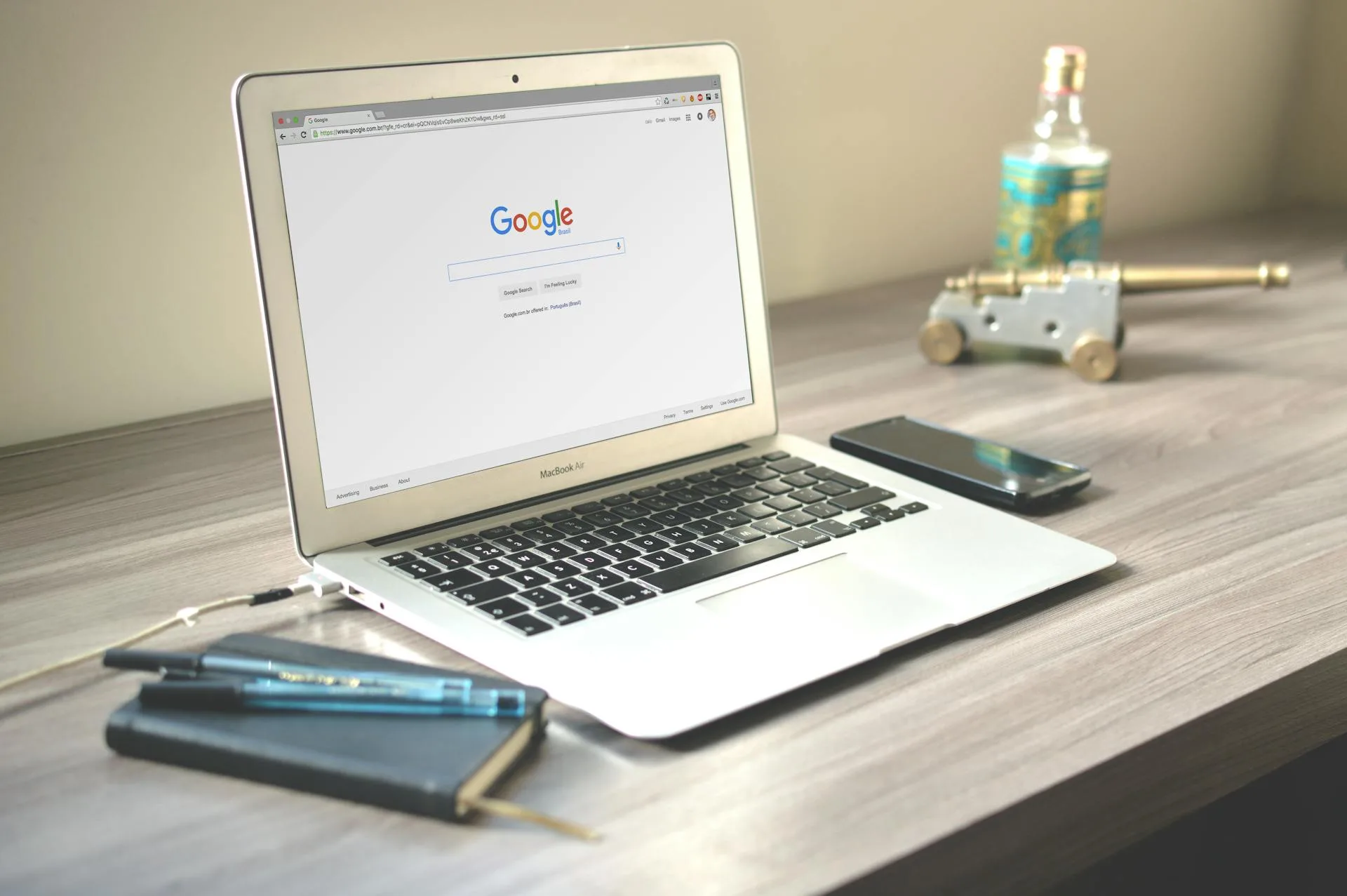 Laptop displaying Google search next to a smartphone and notebook on a wooden desk